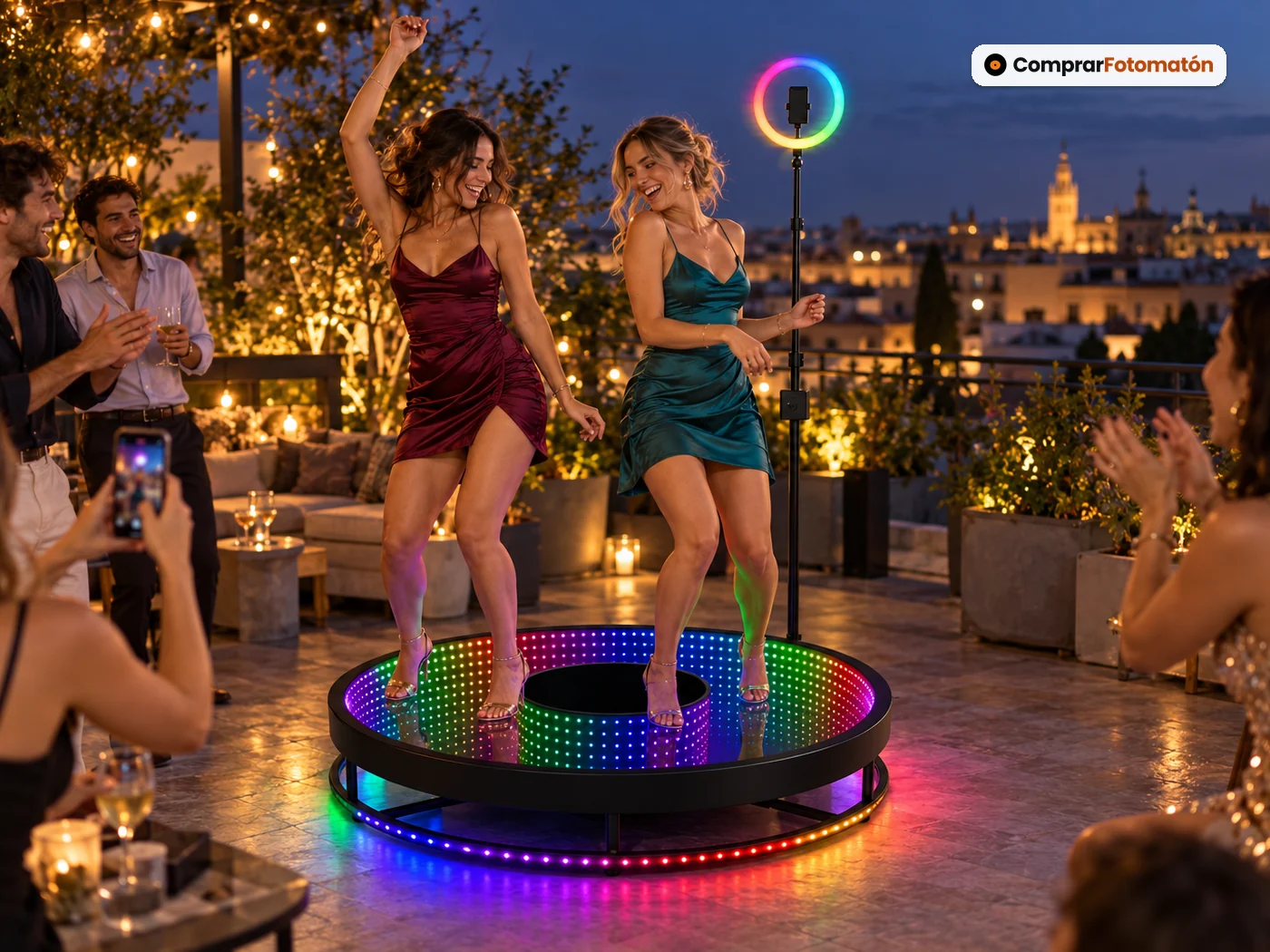 Dos amigas bailando sobre el Fotomatón 360 Espejo Infinito en una azotea al anochecer, con el espejo infinito multicolor bajo sus pies y el aro de luz girando a su alrededor